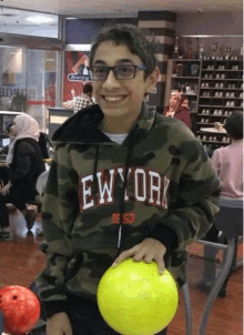 a boy wearing a new york sweatshirt is holding a yellow bowling ball