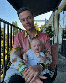 a man in a pink shirt holds a baby in his arms