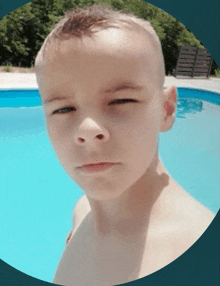 a young boy is standing in front of a swimming pool making a funny face