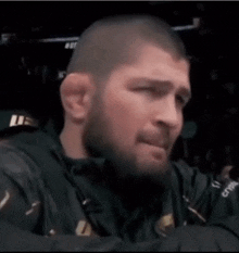 a close up of a man 's face with a beard and a ufc logo on his jacket .