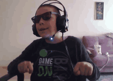 a young boy wearing headphones and sunglasses has a shirt that says game on