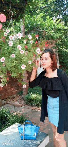 a woman stands in front of a hanging basket of flowers and a blue bag