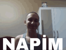 a young man with a shaved head is smiling in front of a sign that says napim