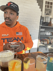 a man wearing a polo team hoodie sits at a table with drinks