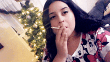 a woman wearing a minnie mouse shirt smoking a cigarette in front of a christmas tree