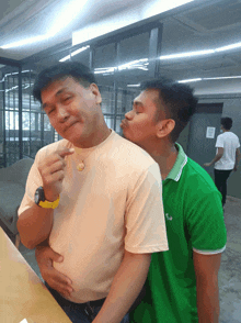 a man in a green polo shirt kisses another man on the neck