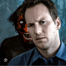 a man in a blue shirt is standing in front of a monster with a red face painted on it