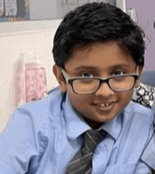 a young boy wearing glasses and a blue shirt and tie is sitting on a couch .