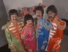 a group of men dressed as the beatles are standing next to each other in a room .