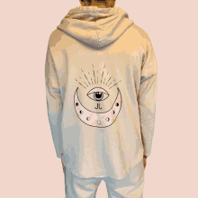 a person wearing a beige hoodie with a pink crescent moon and an eye on it