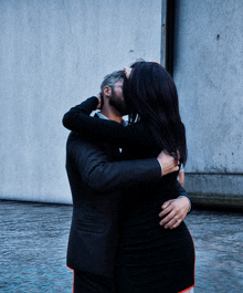 a man in a suit and a woman in a black dress hugging