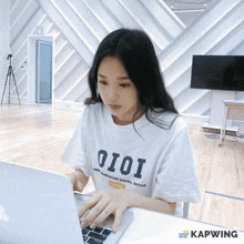 a woman wearing a white t-shirt that says oioi on it is typing on a laptop