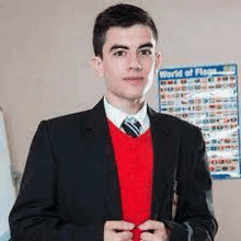 a young man in a suit and red sweater is standing in front of a poster .