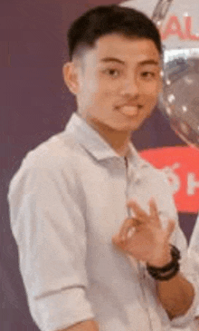 a young man in a white shirt is giving a heart sign while standing in front of balloons .