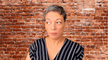 a woman in a black and white striped shirt stands in front of a red brick wall