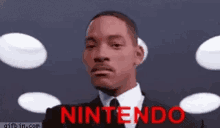 a man in a suit and tie is standing in front of a screen that says nintendo .