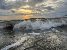 waves crashing on the beach at sunset with a cloudy sky in the background