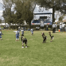 a group of young boys are playing a game of football in a field with a bleachers in the background