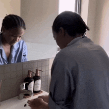 a woman in a blue shirt is washing her hands in front of a mirror with a bottle of vitamin e on the counter