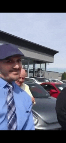 a man wearing a hat and tie stands in front of a car dealership .