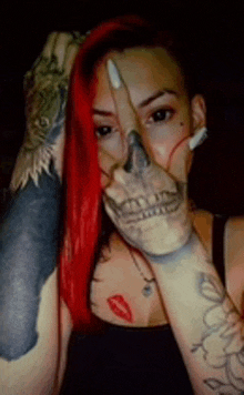 a woman with red hair and a skull tattoo on her hand is covering her face with her hand .