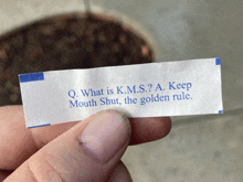 a person is holding a fortune cookie that says q. what is k.m.s.? a. keep mouth shut