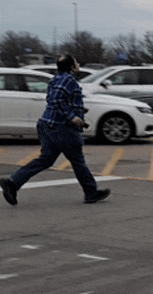 a man in a blue plaid shirt is walking across a parking lot