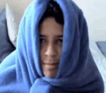 a person wrapped in a blue blanket with their head covered .