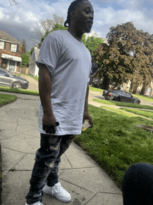 a man in a white shirt is standing on a sidewalk holding a bottle