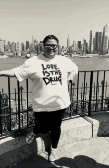 a woman wearing a t-shirt that says love is the drug stands in front of a city skyline