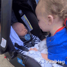 a baby in a car seat is being held by a young boy with the word viralhog on the bottom