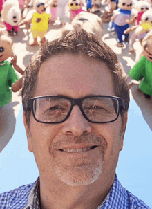 a man wearing glasses and a plaid shirt smiles in front of a bunch of stuffed animals