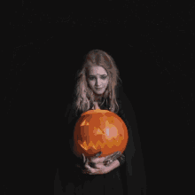 a woman in a witch costume is holding a pumpkin with the words " i wish you a happy halloween "