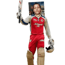 a young boy in a red cricket uniform is holding a bat and helmet .