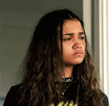 a young woman with long hair is standing in front of a window and making a sad face .