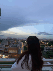 a woman stands on a balcony overlooking a city at sunset