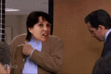 a man and a woman are standing next to each other in an office and the woman is pointing at the man .