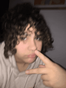 a blurry picture of a person with curly hair pointing to their nose