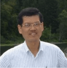 a man wearing glasses and a blue striped shirt is standing in front of a lake .