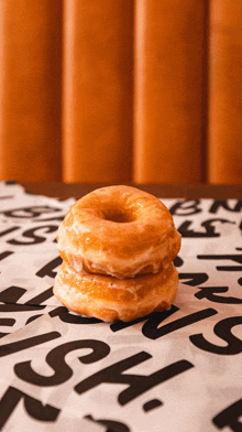 two glazed donuts are stacked on top of each other on a piece of paper with letters on it