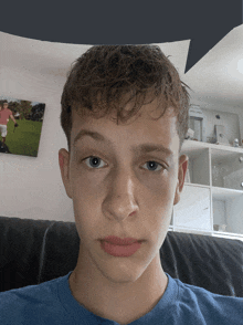 a young man in a blue shirt is sitting on a couch in front of a picture on the wall