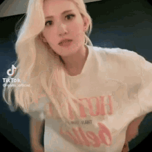 a woman with blonde hair is wearing a white t-shirt with a pink graphic on it .