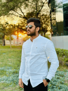 a man wearing sunglasses and a white shirt is standing in a park