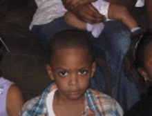 a young boy in a plaid shirt is sitting in a crowd of children