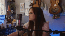 a woman wearing headphones stands in front of a microphone in front of a sign that says one thing