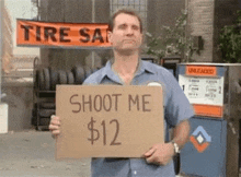 a man is holding a cardboard sign that says `` shoot me $ 12 '' .