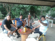 four men sitting around a table with a bottle of skol beer