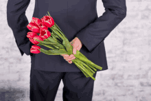 a man in a suit holding a bouquet of red tulips behind his back