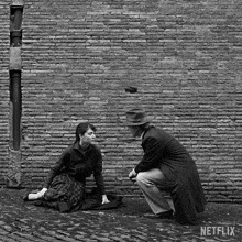 a man and a woman are sitting in front of a brick wall with netflix written on the bottom right