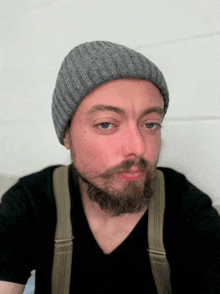 a man with a beard wearing suspenders and a gray beanie